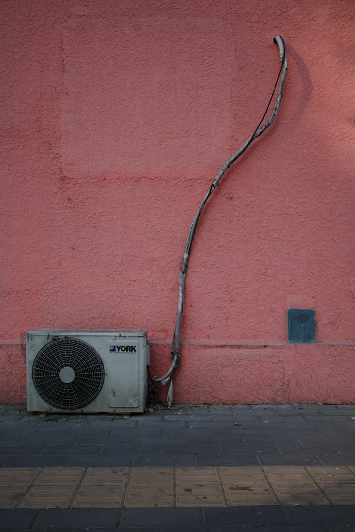 hero-services Air conditioning unit against a pink wall with a sidewalk, showing urban setting.