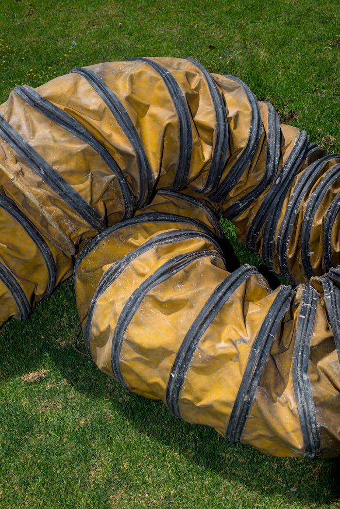 hero-contact Close-up of a coiled yellow industrial ventilation duct resting on green grass.